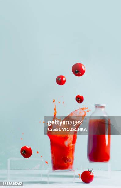 splashing tomato juice in glass, floating tomatoes and glass bottle with juice. pale blue background. creative food levitation - tomatensap stockfoto's en -beelden