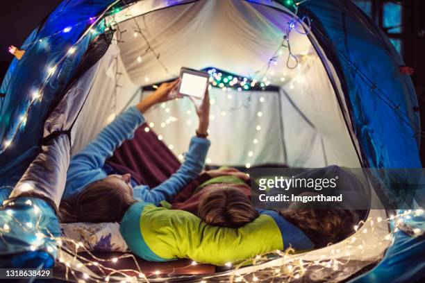 three kids reading e-book together in tent in living room - indoor camping stock pictures, royalty-free photos & images