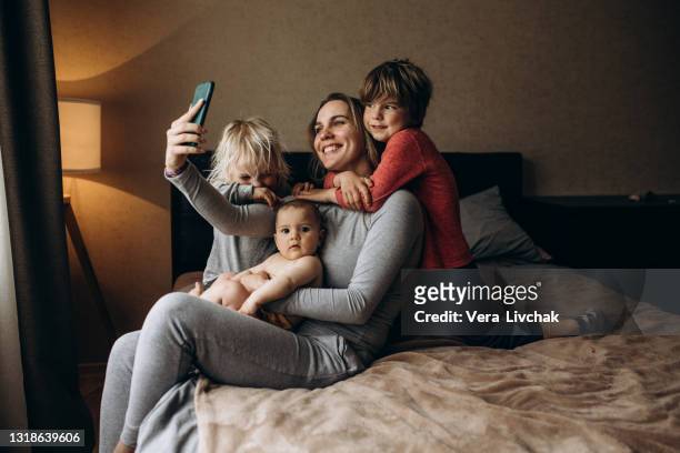 smiling young mother with little preschooler kids sit on couch make self-portrait picture on cell together, happy mother with small children have fun take selfie on smartphone at home - eltern baby stockfoto's en -beelden