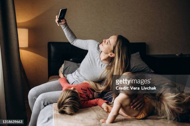smiling young mother with little preschooler kids sit on couch make self-portrait picture on cell together, happy mother with small children have fun take selfie on smartphone at home - eltern stock pictures, royalty-free photos & images