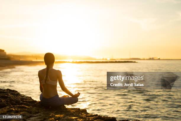 woman meditating on the rocks, by the sea - sunrise yoga stock-fotos und bilder