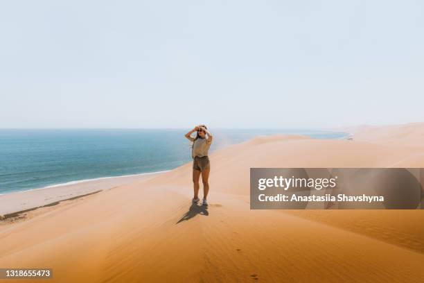 woman staying on the top of the dune at the seacoast exploring the beautiful landscape at sandwich harbour, namibia - namibia women stock pictures, royalty-free photos & images