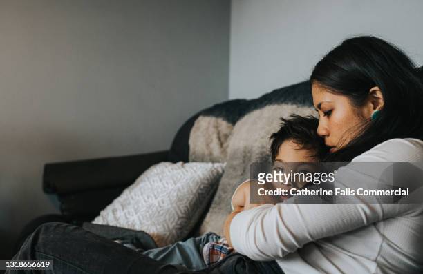 a mother holds her sky little boy close to her chest, and he tenderly rests his head on her - separation anxiety stock pictures, royalty-free photos & images