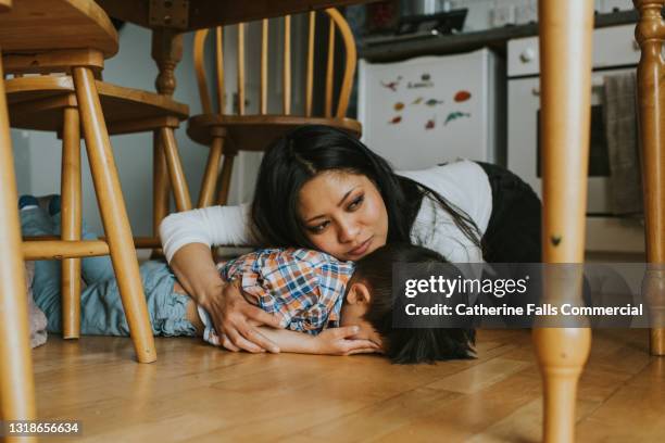 a little boy lies face down on the floor under a table, while a woman comforts him - trotzanfall stock-fotos und bilder