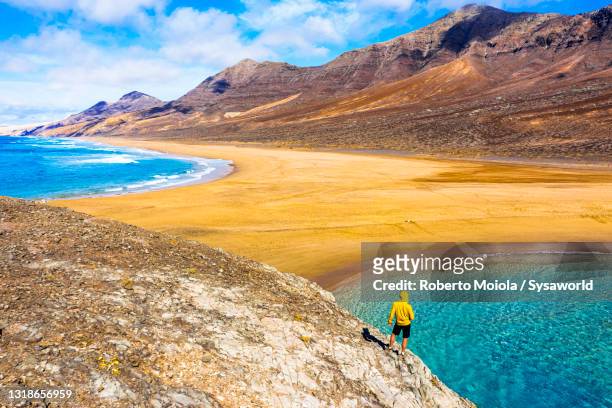 man standing on el islote above crystal sea, fuerteventura - cliff shore stock-fotos und bilder