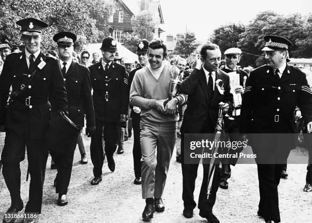 Tony Jacklin of Great Britain walks back to the clubhouse holding the Champion Golfer Claret Jug trophy with a police escort after winning the 98th...