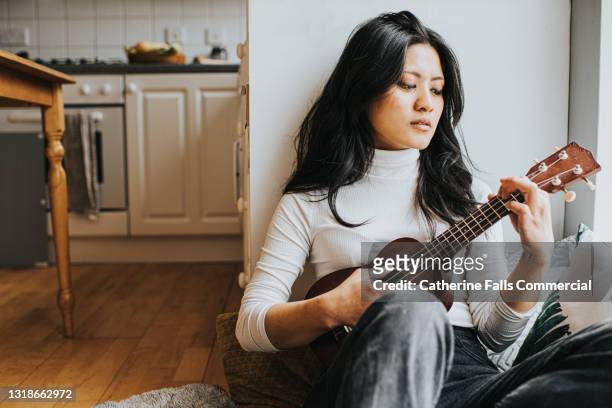 a woman plays a ukulele in a domestic environment - songwriter stock pictures, royalty-free photos & images