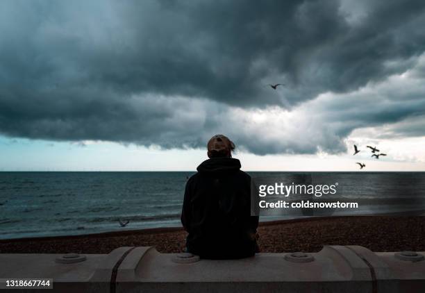 eenzame mens die de overzeese en onweerswolken bekijkt - thinking man cloud stockfoto's en -beelden