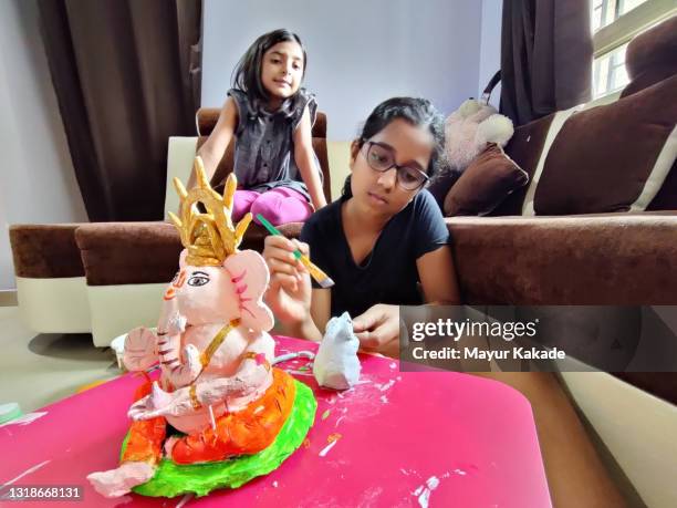 girl making a clay statue of hindu god ganesha with her younger sister sitting besides her - taken on mobile device stock pictures, royalty-free photos & images