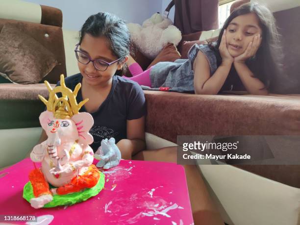 girl making a clay hindu god statue with her younger sister sitting besides her - ganesh chaturthi fotografías e imágenes de stock