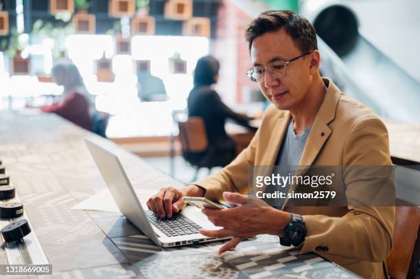 an asian businessman received message while working on laptop in a co-working space - co op stock pictures, royalty-free photos & images