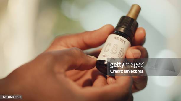 medical marijuana research. african scientist holding glass bottle with cbd oil - cbd oil stock pictures, royalty-free photos & images