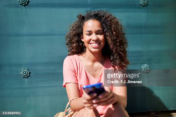 woman with afro hair using smart phone on the street - junge frau allein stock-fotos und bilder