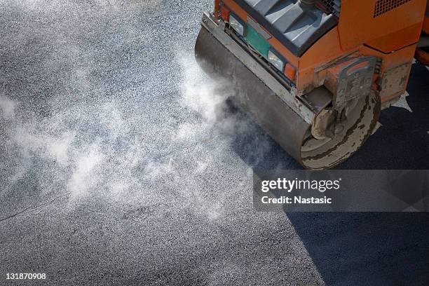 a roller compacting asphalt on a road - way of working stockfoto's en -beelden