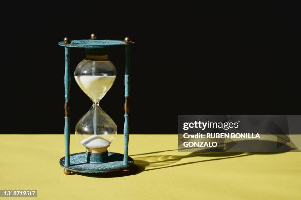 antique blue hourglass time with sand running through against black and yellow background - antique clocks stock-fotos und bilder