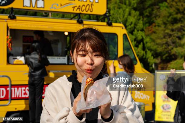 junge frau genießt wirklich einen leckeren snack aus einem food-truck - schuldig stock-fotos und bilder