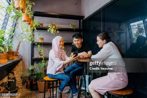 asian office workers using smartphone and having discussion - malayan ethnicity stock pictures, royalty-free photos & images