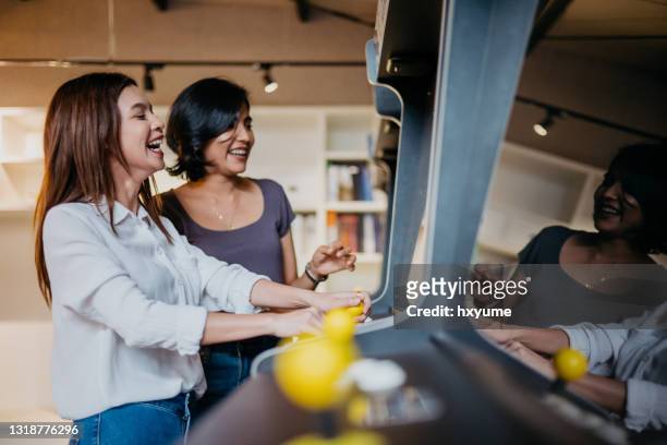 young asian woman playing vintage arcade video game in office games room - video arcade imagens e fotografias de stock