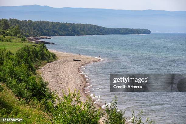 Tourists paddling and sunning on pebble beach at Lake Baikal, rift lake in southern Siberia, Russia.