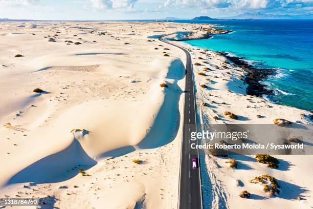 car on empty road crossing desert dunes, fuerteventura - corralejo stock-fotos und bilder