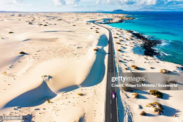 car on empty road crossing desert dunes, fuerteventura - fuerteventura strand stock-fotos und bilder