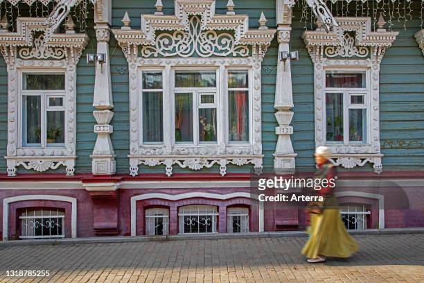 Russian woman walking in front of traditional ornate wooden house in the city Perm, Perm Krai, Russia.