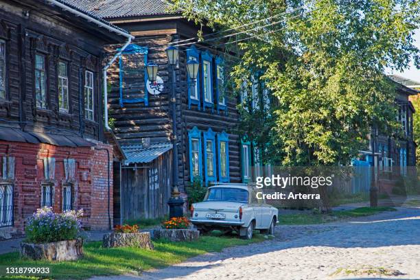Cobbled street with classic Soviet Moskvich 408 car and traditional Siberian wooden houses in Tomsk Oblast, Siberia, Russia.