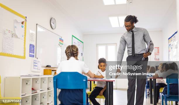 primary school teacher and students in classroom. teacher distributing a educational exam - grade 4 stock pictures, royalty-free photos & images