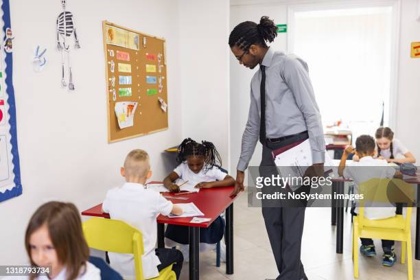 primary school teacher and students in classroom. teacher distributing a educational exam - grade 4 stock pictures, royalty-free photos & images