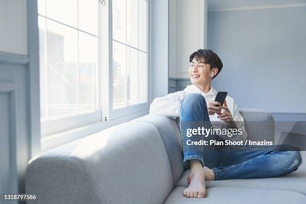 a man using audio application through smartphone - jeans barefoot fotografías e imágenes de stock