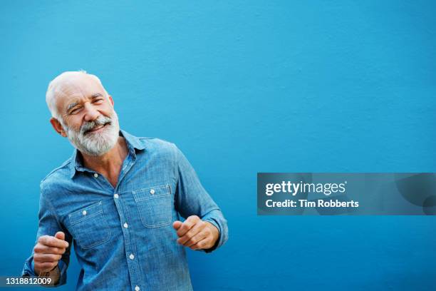 happy man dancing next to blue wall, outside - coloured background stock-fotos und bilder