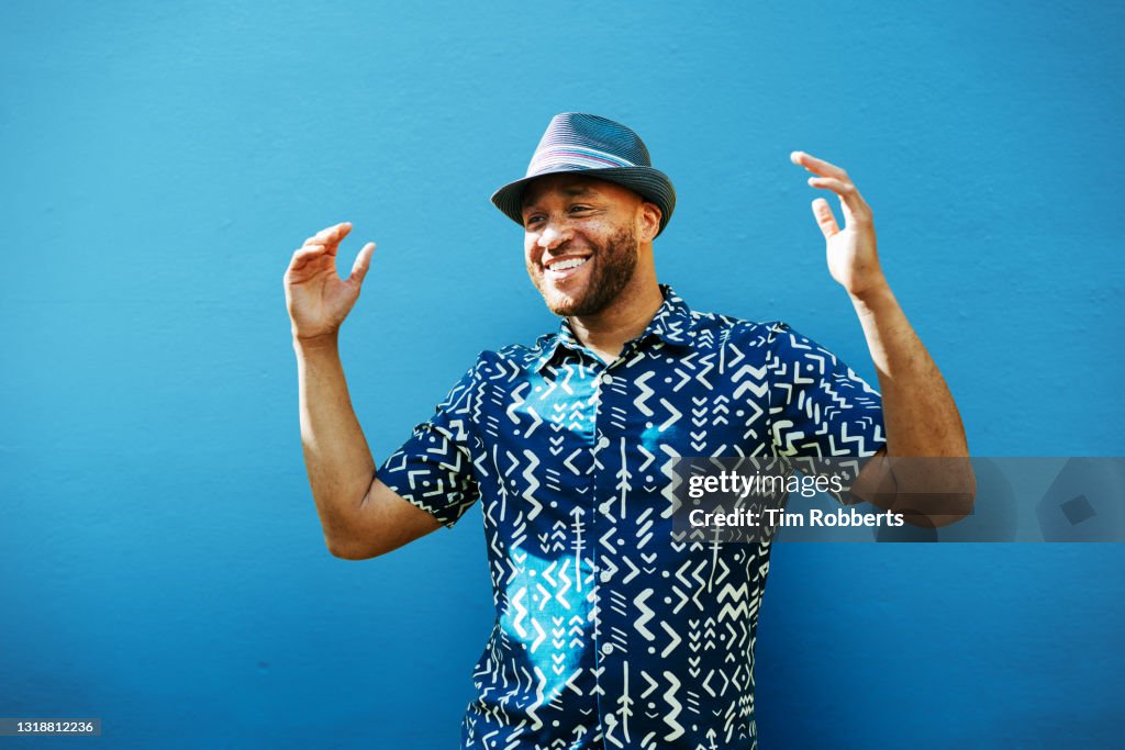 Man with arms up, smiling, next to blue wall