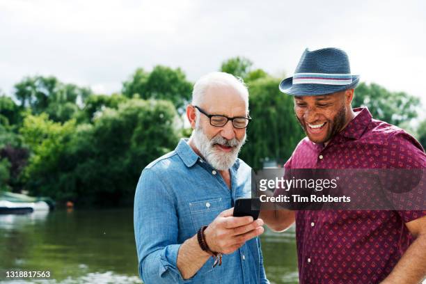 two men sharing smart phone and smiling - generation x stock pictures, royalty-free photos & images