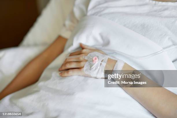 sick female lying on bed in icu during covid-19 - iv drip womans hand stock-fotos und bilder