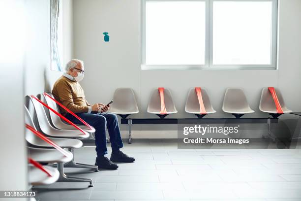 patient using mobile phone in waiting room - coronavirus mask stockfoto's en -beelden