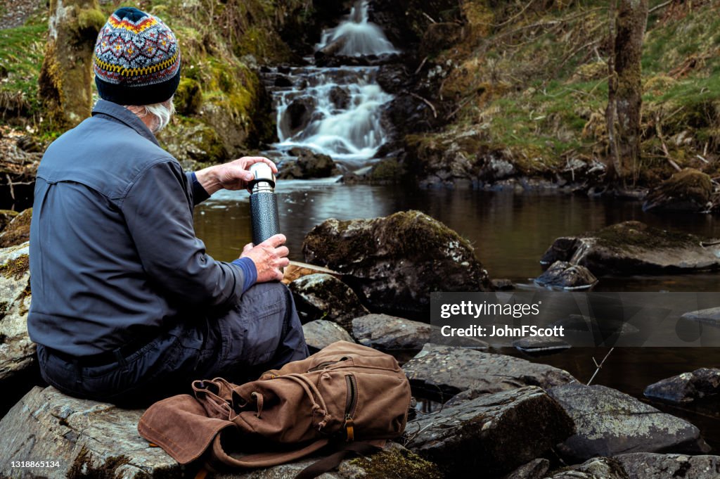 Hogere mens met een thermosfles bij een waterval