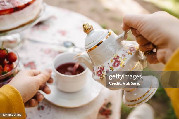 frau, die tee aus einer teekanne in eine teetasse gießt - teegesellschaft stock-fotos und bilder