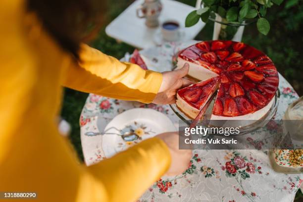 frau, die eine scheibe eines erdbeer-käsekuchens schneidet - fruit cake stock-fotos und bilder