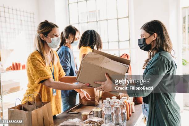 a millennial woman is taking a box of food and drink at the food and clothes bank - food staple stock pictures, royalty-free photos & images