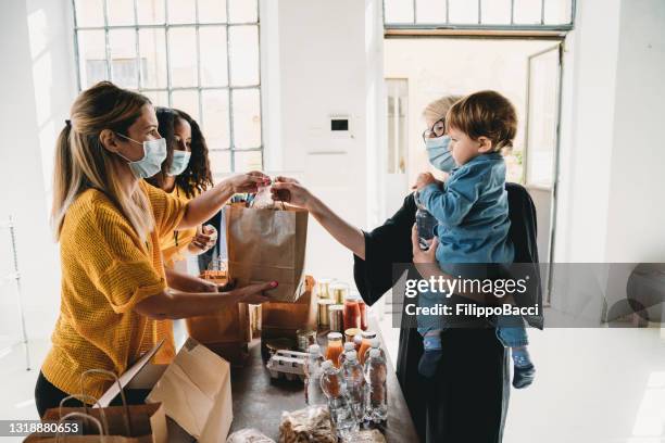 a mother with her little son is taking a bag of food at the food and clothes bank - group of people wearing masks stock pictures, royalty-free photos & images