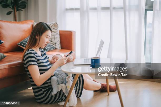 aziatische chinese mooie vrouw die van huis met behulp van laptop die haar babyjongen in woonkamer draagt - stay at home mother stockfoto's en -beelden