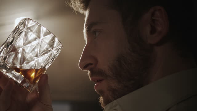 A backstage video with a view from over the shoulder of a man who drinks whiskey from the glass in a bright light of the spotlight