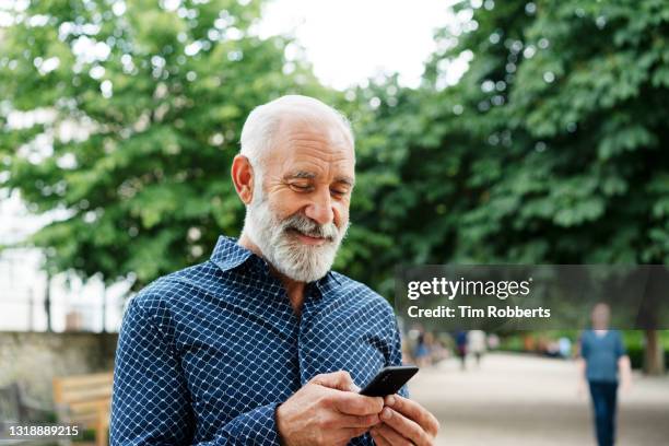 man using smart phone in park - rentner mann allein lustig stock-fotos und bilder