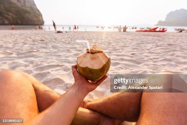 man relaxing on the beach and drinking fresh coconut water personal perspective view (pov) - coconut water stock pictures, royalty-free photos & images