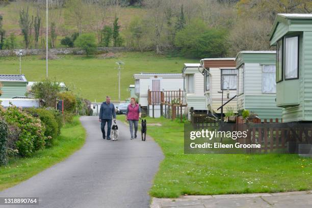 ウェールズの田舎で休暇を楽しんでいる春の日に、静的なキャラバンが両側に駐車しているキャラバンサイトの周りで犬を歩いているカップル。 - トレーラハウス ストックフォトと画像