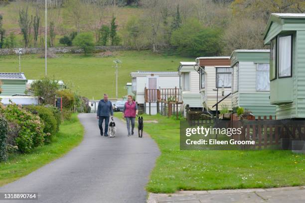 couple walking their dogs around a caravan site with static caravans parked either side on a spring day enjoying a vacation in rural wales uk. - trailer home stock pictures, royalty-free photos & images