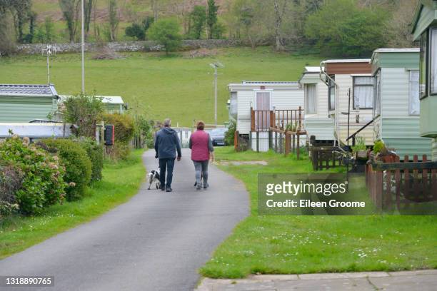 couples marchant leurs chiens autour d’un emplacement de caravane avec des caravanes statiques garées de chaque côté un jour de printemps appréciant des vacances dans le pays de galles rural r-u. - caravan uk photos et images de collection