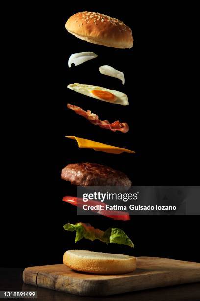 hamburger toppings flying on black background on a wooden board - burger stock pictures, royalty-free photos & images