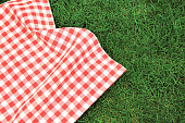 000Red picnic  towel on green grass top view, checked cloth flat lay. Food advertisement display.