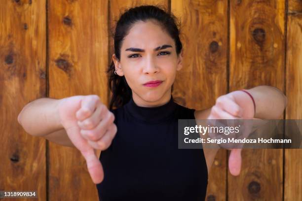 young latino woman looking at the camera and giving a thumbs down - daumen runter stock-fotos und bilder